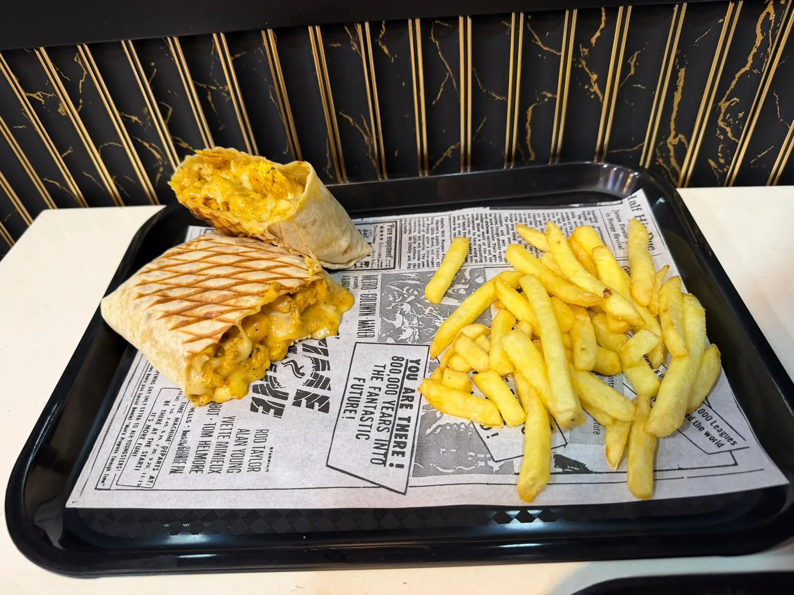 Taco francés de pollo partido por la mitad, con queso fundido, junto a papas fritas.