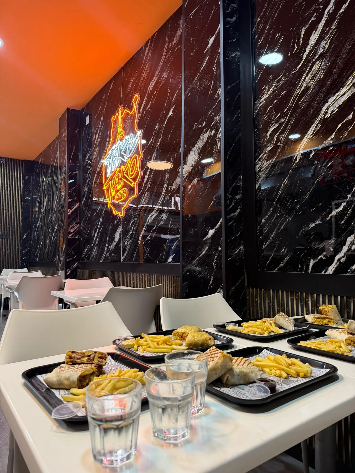 Interior de Tiki Tako con paredes de mármol negro, techo naranja y el neón del logo.